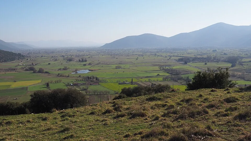 Low archaeological remains of ancient Mantineia amid fields and distant mountains.