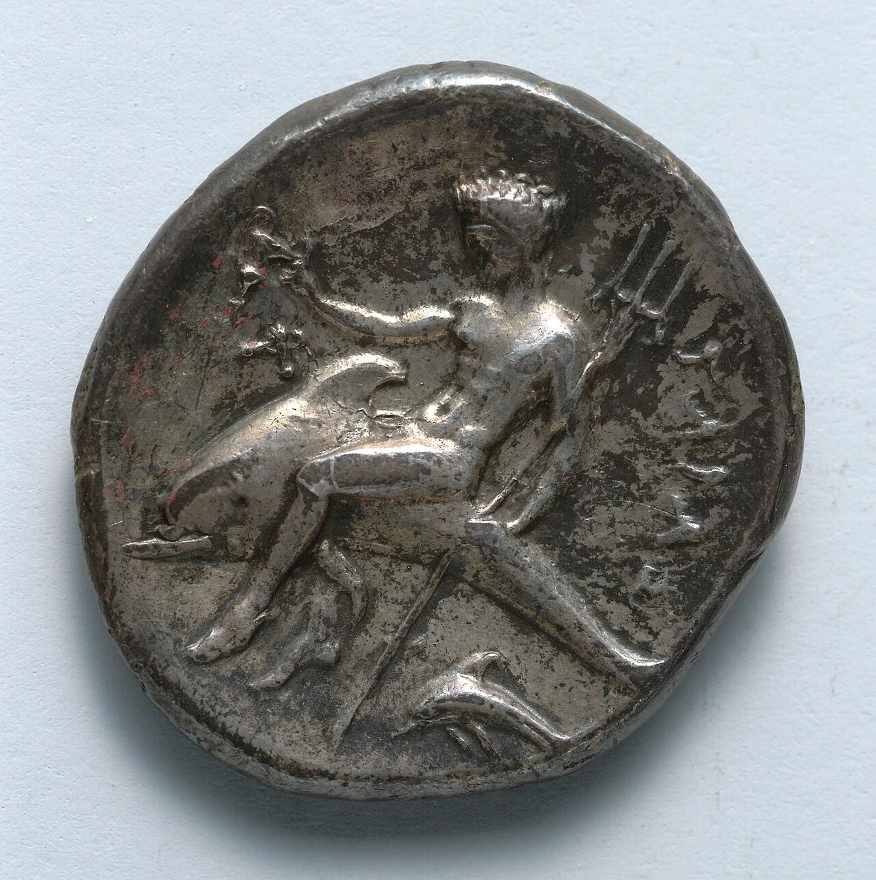 Silver coin showing a mythical youth riding a dolphin and holding a trident